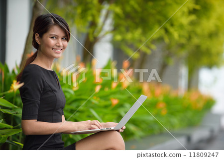 Successful young Malay business woman using laptop along promenade during break time Successful young Malay business woman using laptop along promenade during break time 11809247