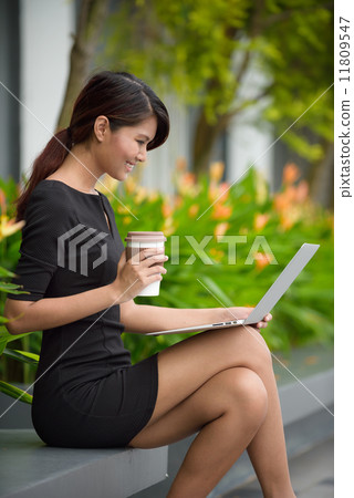 Successful young Malay business woman with coffee cup and laptop along promenade during break time Successful young Malay business woman with coffee cup and laptop along promenade during break time 11809547