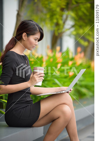 Successful young Malay business woman with coffee cup and laptop along promenade during break time Successful young Malay business woman with coffee cup and laptop along promenade during break time 11809579