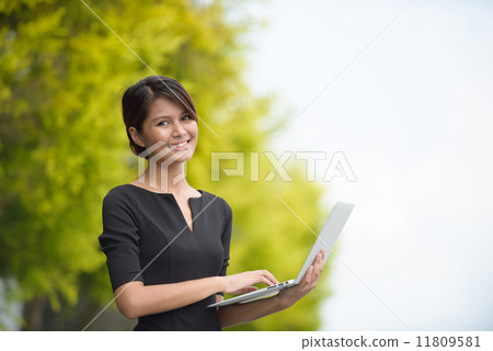 Victorious successful young Malay business woman using laptop along promenade Victorious successful young Malay business woman using laptop along promenade 11809581