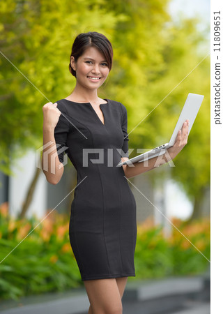 Victorious successful young Malay business woman using laptop along promenade 11809651