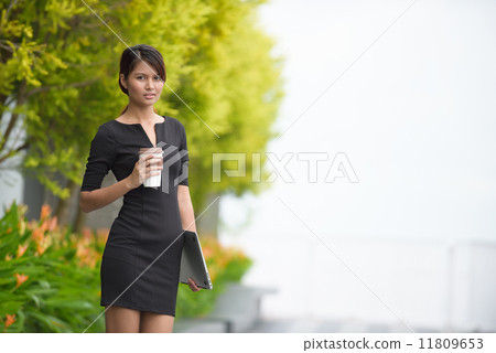 Successful young Malay business woman with coffee cup and laptop along promenade during break time Successful young Malay business woman with coffee cup and laptop along promenade during break time 11809653