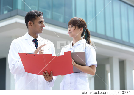 Successful young mixed race medical doctor and nurse in discussion in front of hospital 11810725