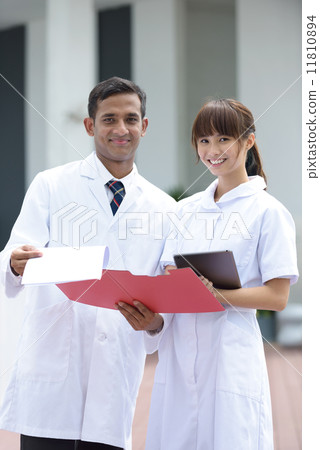 Successful young mixed race medical doctor and nurse in discussion in front of hospital Successful young mixed race medical doctor and nurse in discussion in front of hospital 11810894