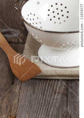 Enamel colander and a Cooking spoon stands on the kitchen table 11859577
