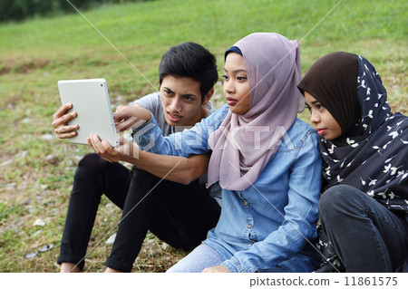 Three Asians watching tablets in the park 11861575