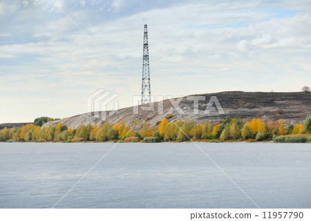 High voltage line and electricity pylon on coastline of river. 11957790