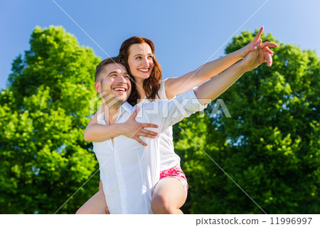 Man carrying woman piggyback in park Man carrying woman piggyback in park 11996997