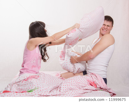 Young couple in bed arranged a pillow fight Young couple in bed arranged a pillow fight 11999675