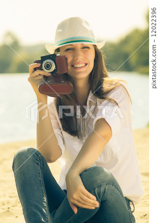 Young woman posing with old film camera. Caucasian hipster girl in hat 12022396