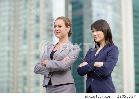 Two young successful business women folding arms standing in front of glass office building Two young successful business women folding arms standing in front of glass office building 12059537