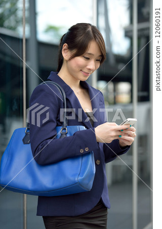 One young successful Chinese business woman using smart phone in front of glass building 12060191
