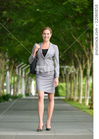One young successful caucasian business woman with hand bag walking along green walkway 12060858