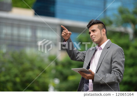 One successful Malay business man along promenade with tablet iPad pointing at his next development 12065164