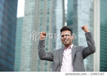 Victorious young successful Malay business man punching fist in the air in front of office building Victorious young successful Malay business man punching fist in the air in front of office building 12065167