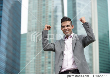 Victorious young successful Malay business man punching fist in the air in front of office building Victorious young successful Malay business man punching fist in the air in front of office building 12065456