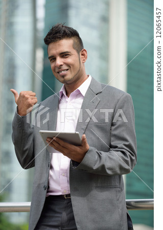 One successful Malay business man with tablet iPad giving thumbs up in front of office building One successful Malay business man with tablet iPad giving thumbs up in front of office building 12065457