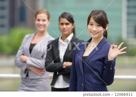 Team leader of 3 young successful mixed race business women giving okay sign in front of office Team leader of 3 young successful mixed race business women giving okay sign in front of office 12066911