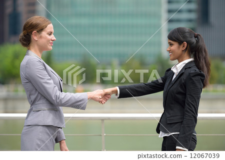 Two successful young mixed race business women shaking hands in front of office buildings  12067039