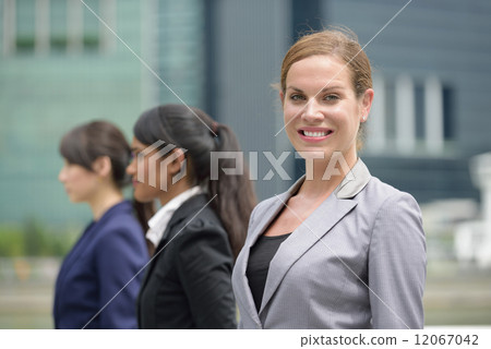 Team leader of three young successful mixed race business women standing in front of office building 12067042