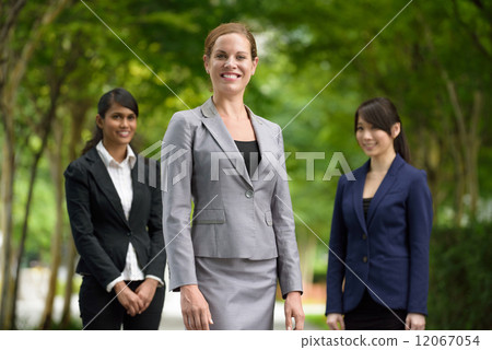 Three young successful multi culture mixed race business women standing along green walkway 12067054