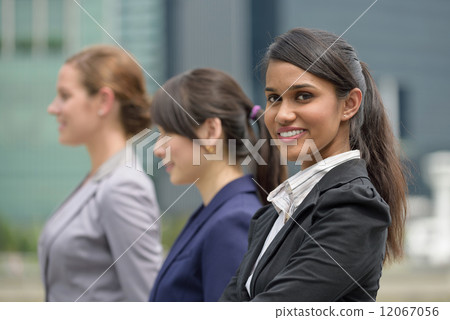 Team leader of 3 young successful mixed race business women standing in front of office building  12067056