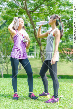 Two young and beautiful ladies taking a break / resting by drinking or hydrating with water 12073748