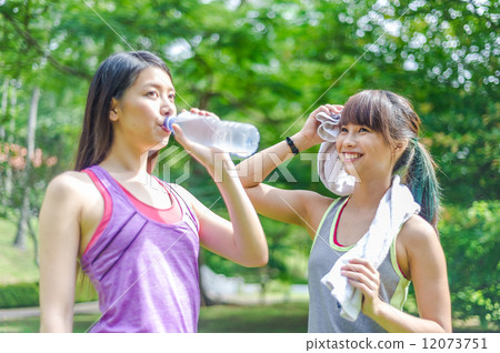 Two young and beautiful ladies taking a break / resting by drinking or hydrating with water Two young and beautiful ladies taking a break / resting by drinking or hydrating with water 12073751
