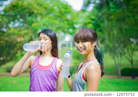 Two young and beautiful ladies taking a break / resting by drinking or hydrating with water 12073752
