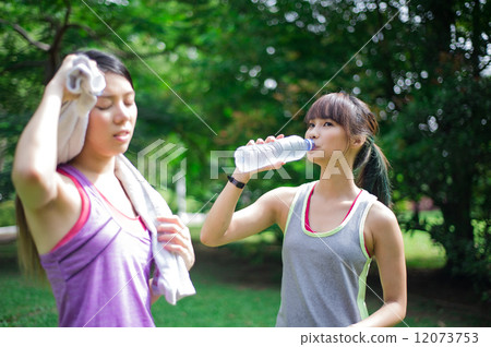 Two young and beautiful ladies taking a break / resting by drinking or hydrating with water 12073753