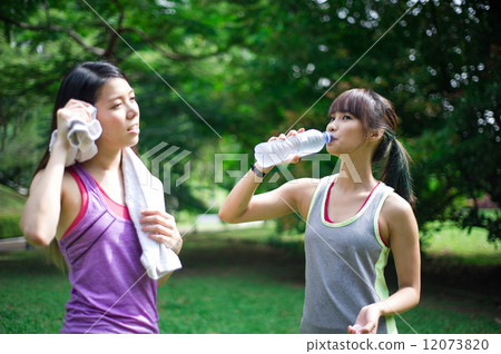 Two young and beautiful asian ladies taking a break from exercise by hydrating with water  12073820