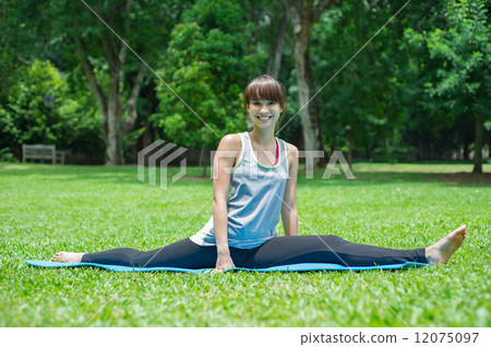 A smiling young and beautiful Asian lady doing yoga on a yoga mat in the garden 12075097
