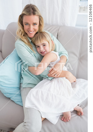 Mother sitting on the couch with her daughter smiling at camera 12106466