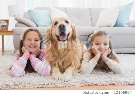 Sisters lying on rug with golden retriever smiling at camera Sisters lying on rug with golden retriever smiling at camera 12106994