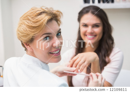 Pretty nail technician giving manicure to customer Pretty nail technician giving manicure to customer 12109811