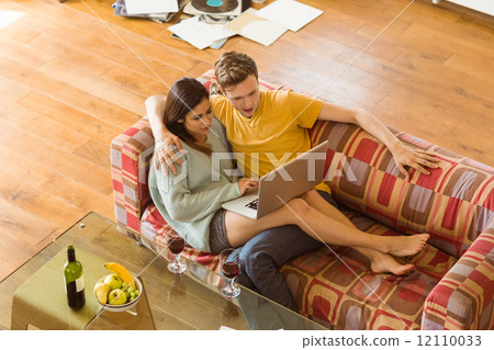 Young couple cuddling on the couch with laptop 12110033