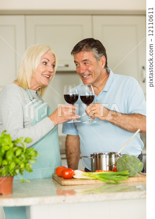 Happy mature couple having red wine while making dinner Happy mature couple having red wine while making dinner 12110611