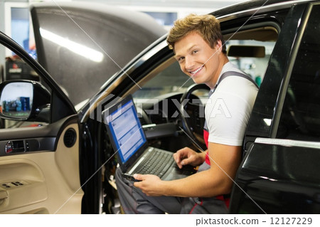 Serviceman making car diagnostics with laptop in a workshop Serviceman making car diagnostics with laptop in a workshop 12127229