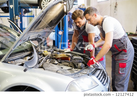 Two mechanics fixing car in a workshop Two mechanics fixing car in a workshop 12127412