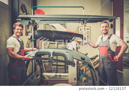 Two workers with car bodykit ready for painting in a workshop Two workers with car bodykit ready for painting in a workshop 12128137