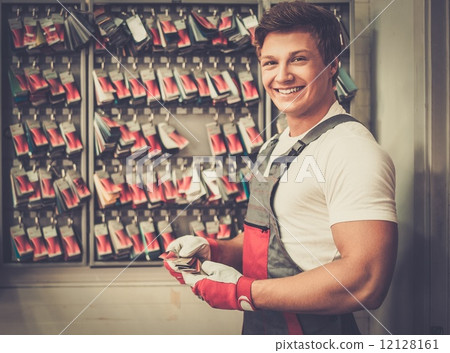 Cheerful serviceman near stand with colour samples in car body workshop 12128161