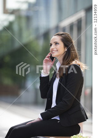 Young Caucasian businesswoman standing outside using mobile phon 12134959