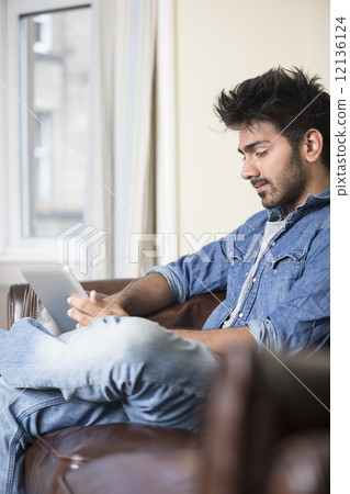 Indian man using digital tablet at home. 12136124