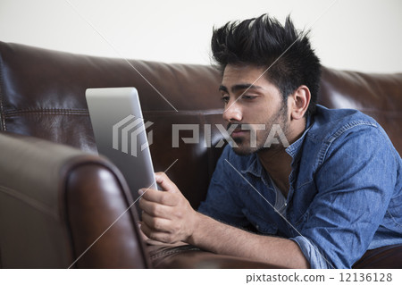 Happy Asian man using digital tablet at home on sofa. Happy Asian man using digital tablet at home on sofa. 12136128