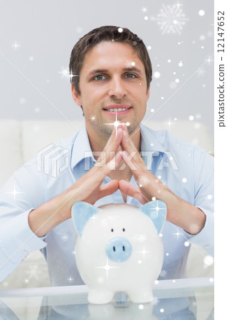 Composite image of handsome casual man with piggy bank in living Composite image of handsome casual man with piggy bank in living 12147652