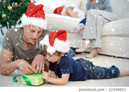 Father and son unwrapping a present lying on the floor 12149921