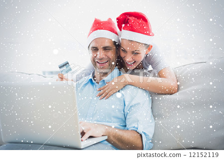 Smiling couple in santa hats shopping online with laptop Smiling couple in santa hats shopping online with laptop 12152119