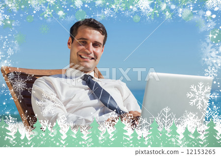 Cheerful young businessman lying on a deck chair with his comput 12153265