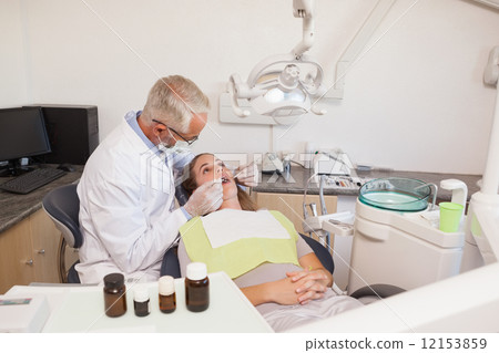 Dentist examining a patients teeth in the dentists chair 12153859