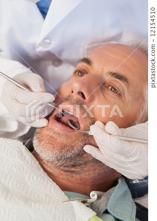 Dentist examining a patients teeth in the dentists chair 12154510